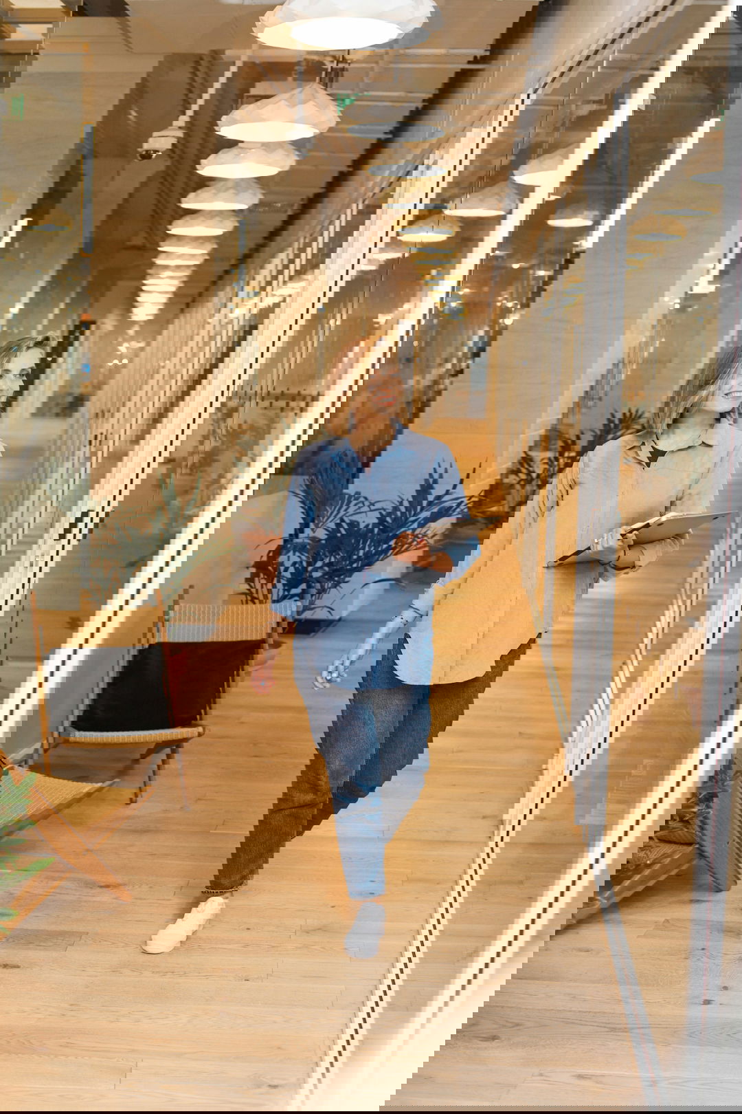 woman in blue dress shirt and blue denim jeans standing beside brown wooden chair